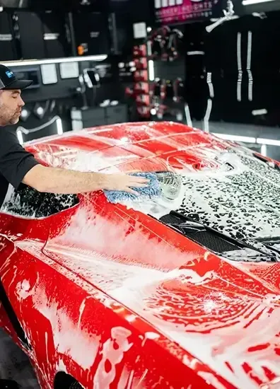 A man is washing a red sports car with soap and water.