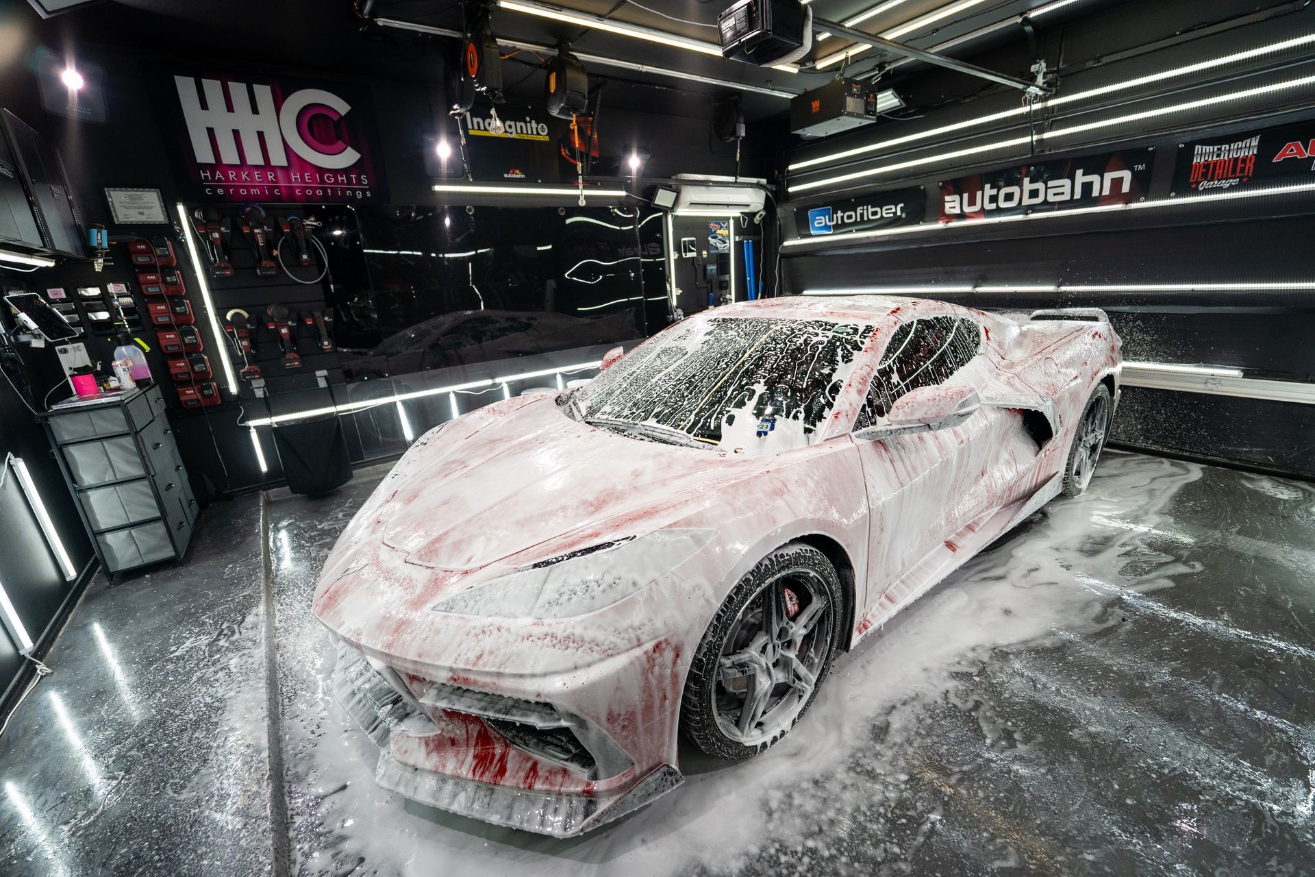 A white sports car is covered in foam in a garage.