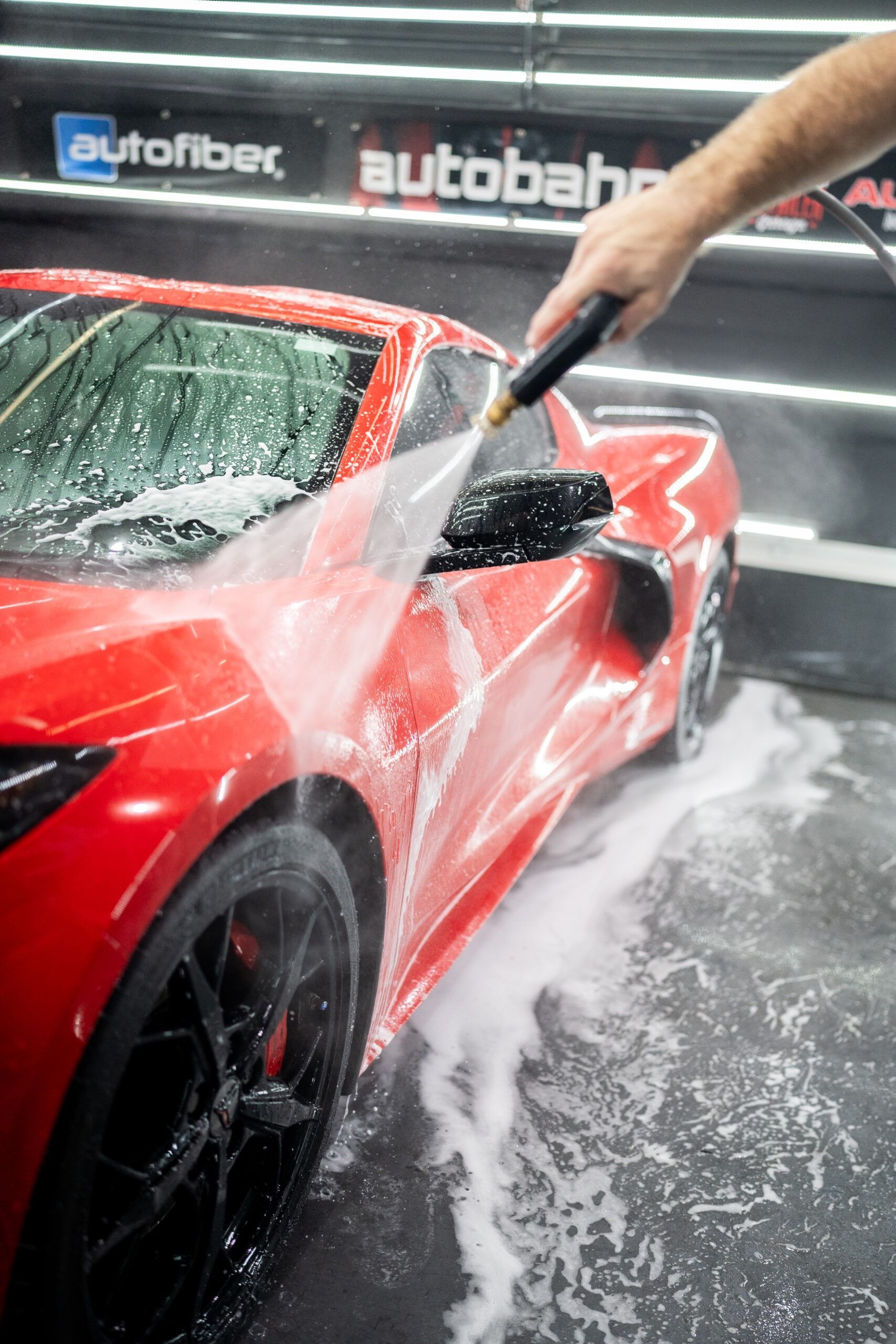 A person is washing a red sports car with a high pressure washer.