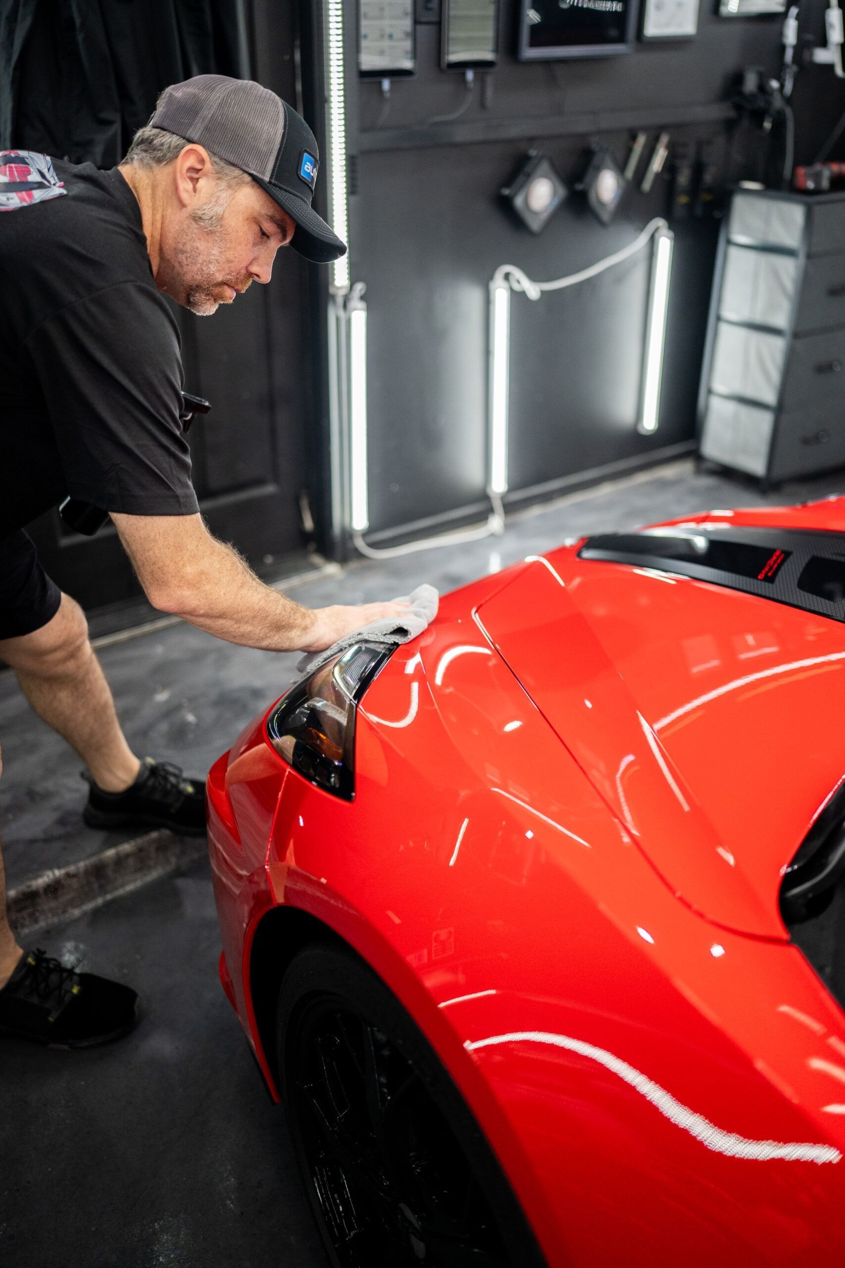 A man is polishing a red sports car in a garage.