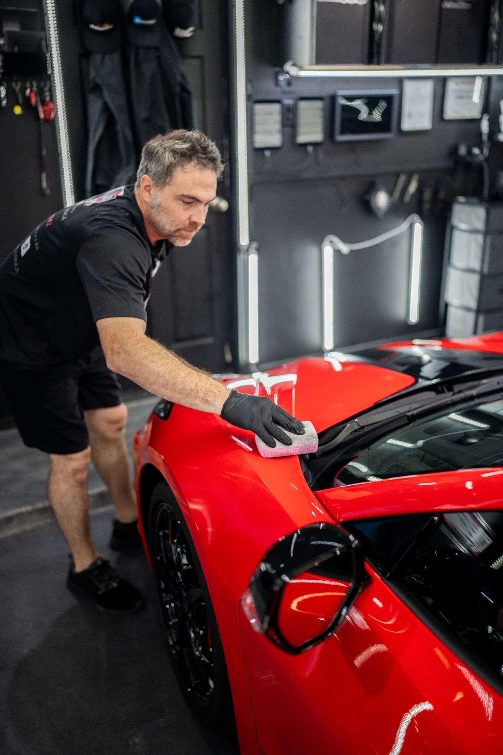 A man is polishing a red sports car in a garage.