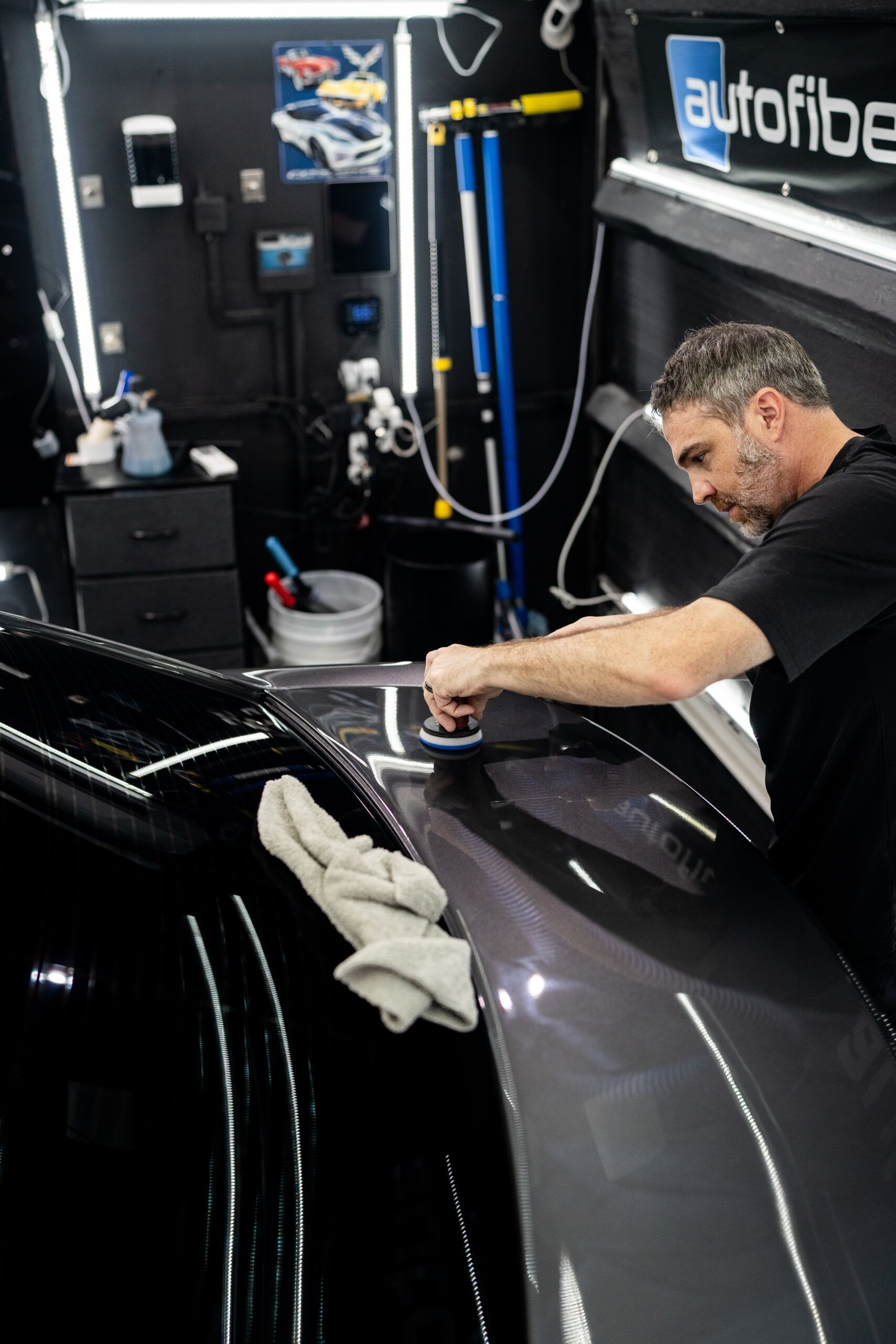 A man is polishing the hood of a car in a garage.