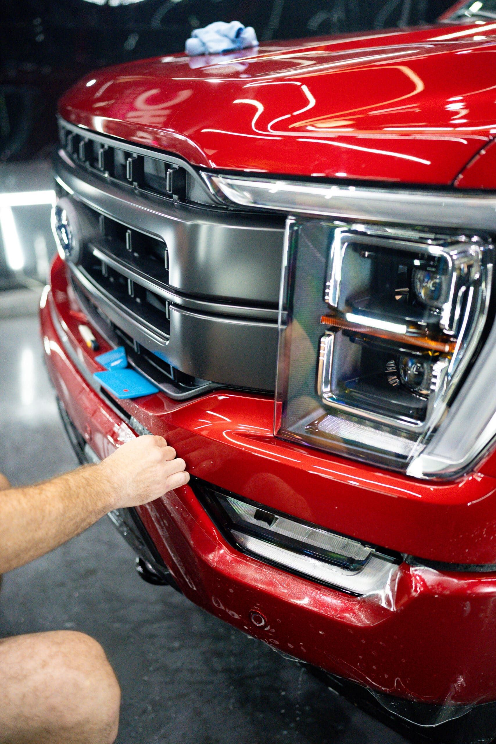 A man is applying a protective film to the front of a red truck.