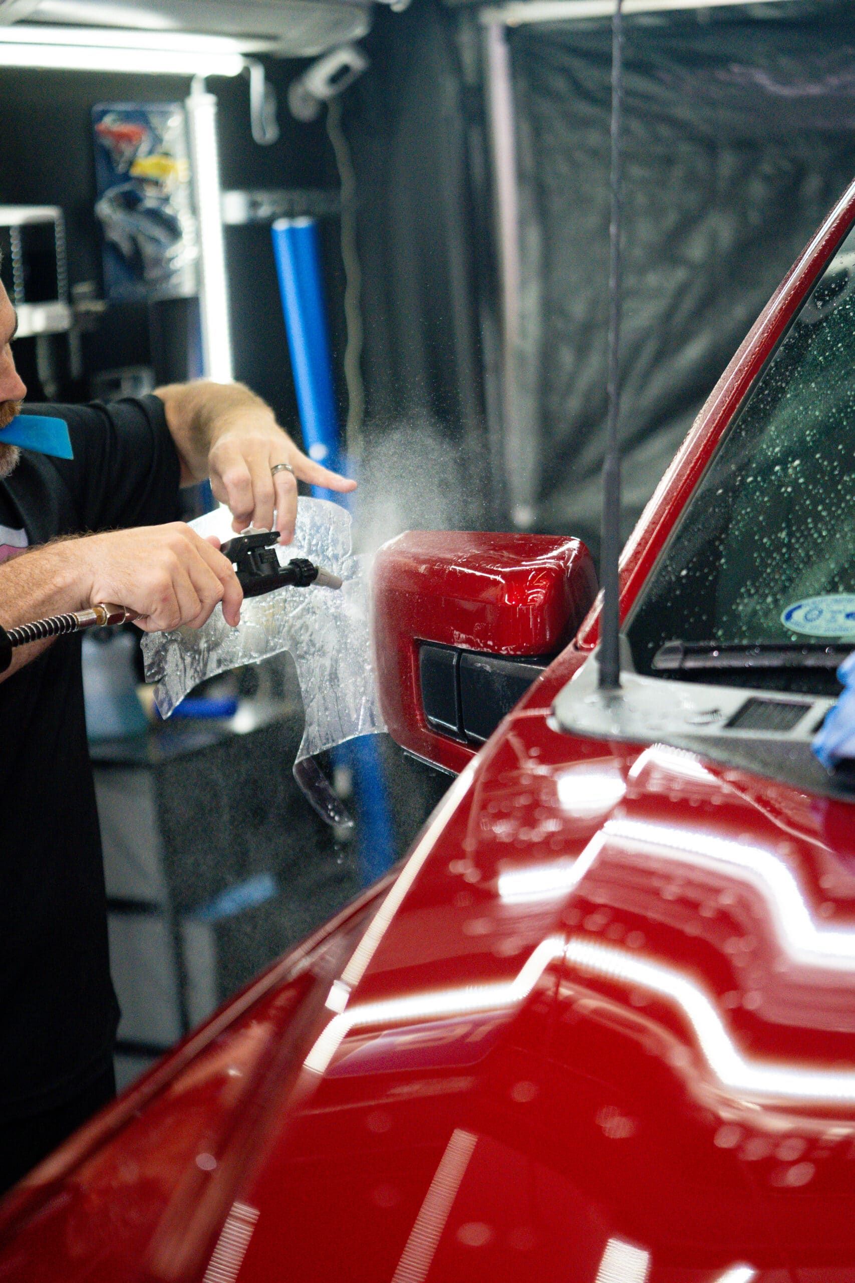 A man is spraying a red car with a spray bottle.