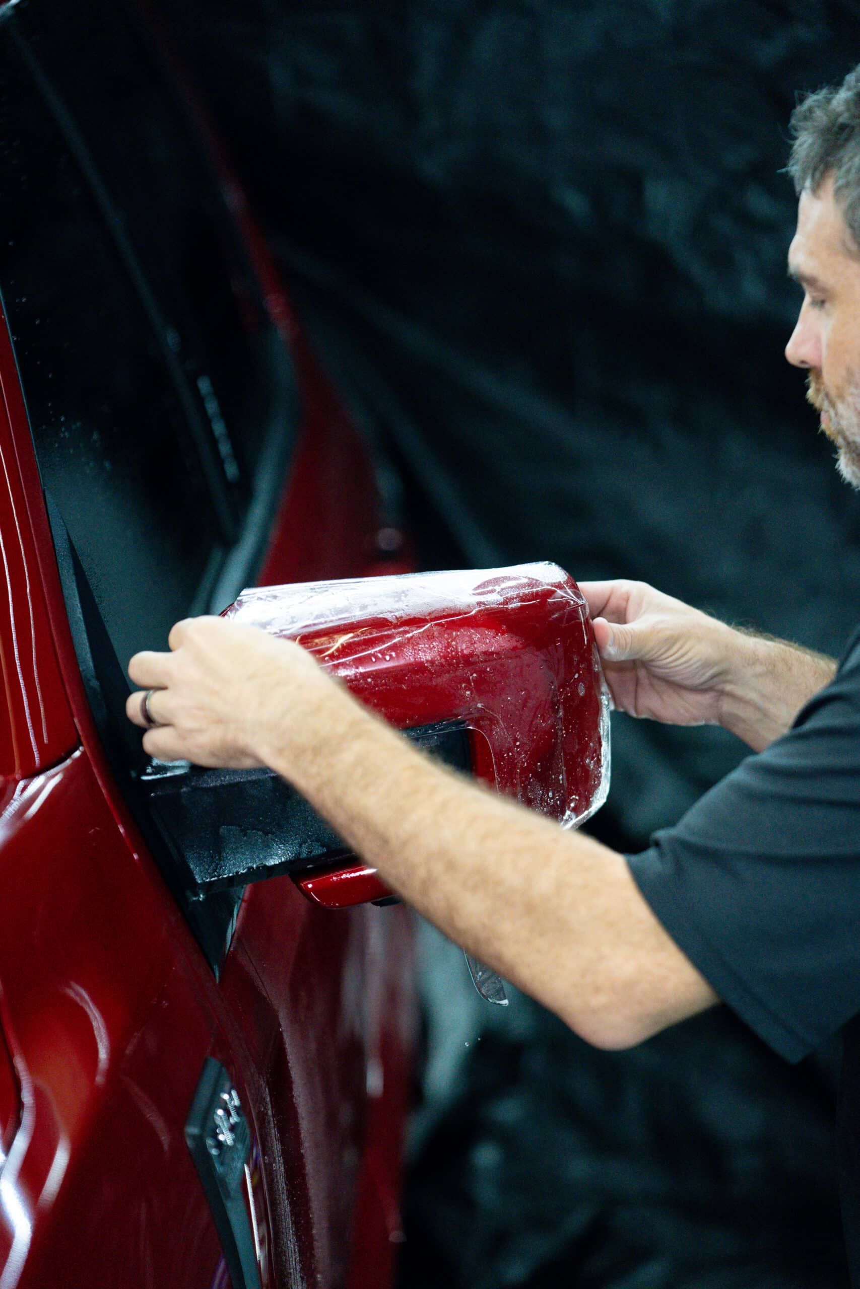 A man is cleaning a red car with a cloth.