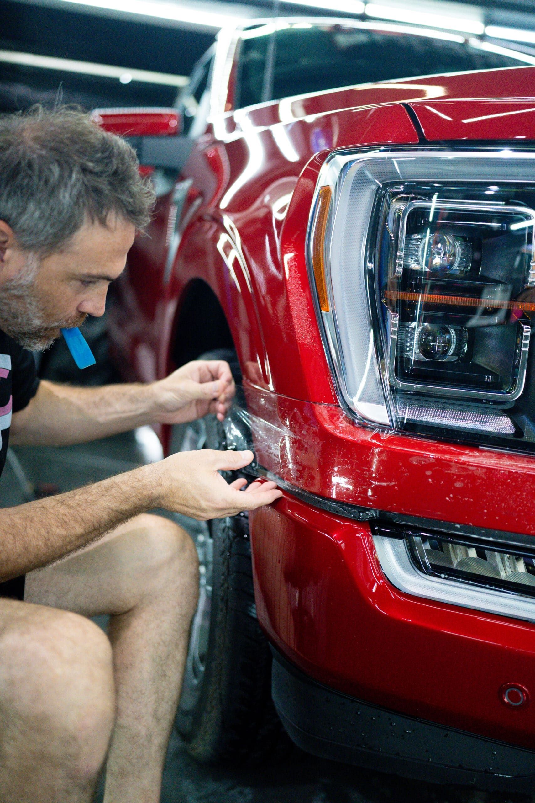 A man is applying a protective film to the front of a red truck.