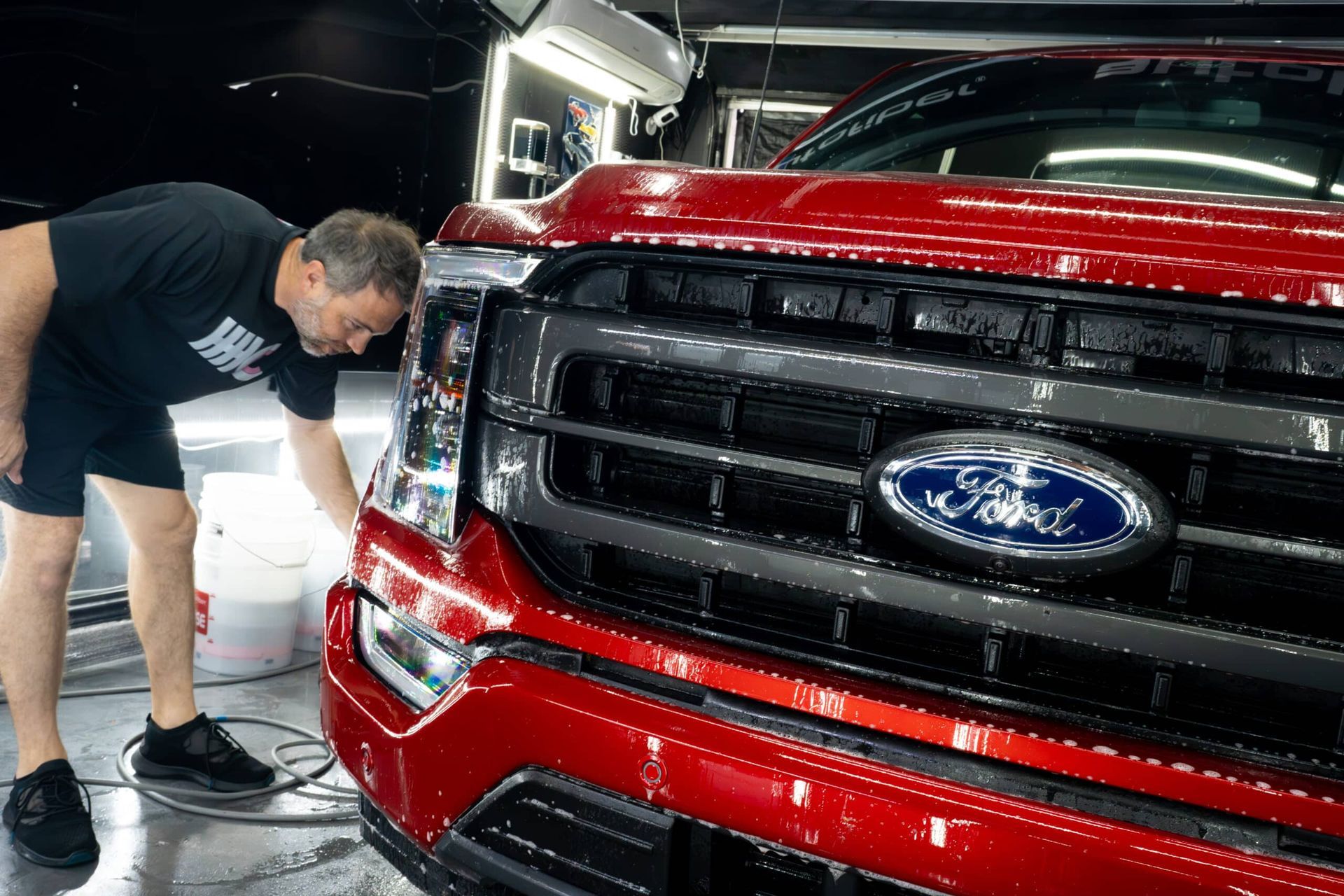 A man is looking at the front of a red ford truck.