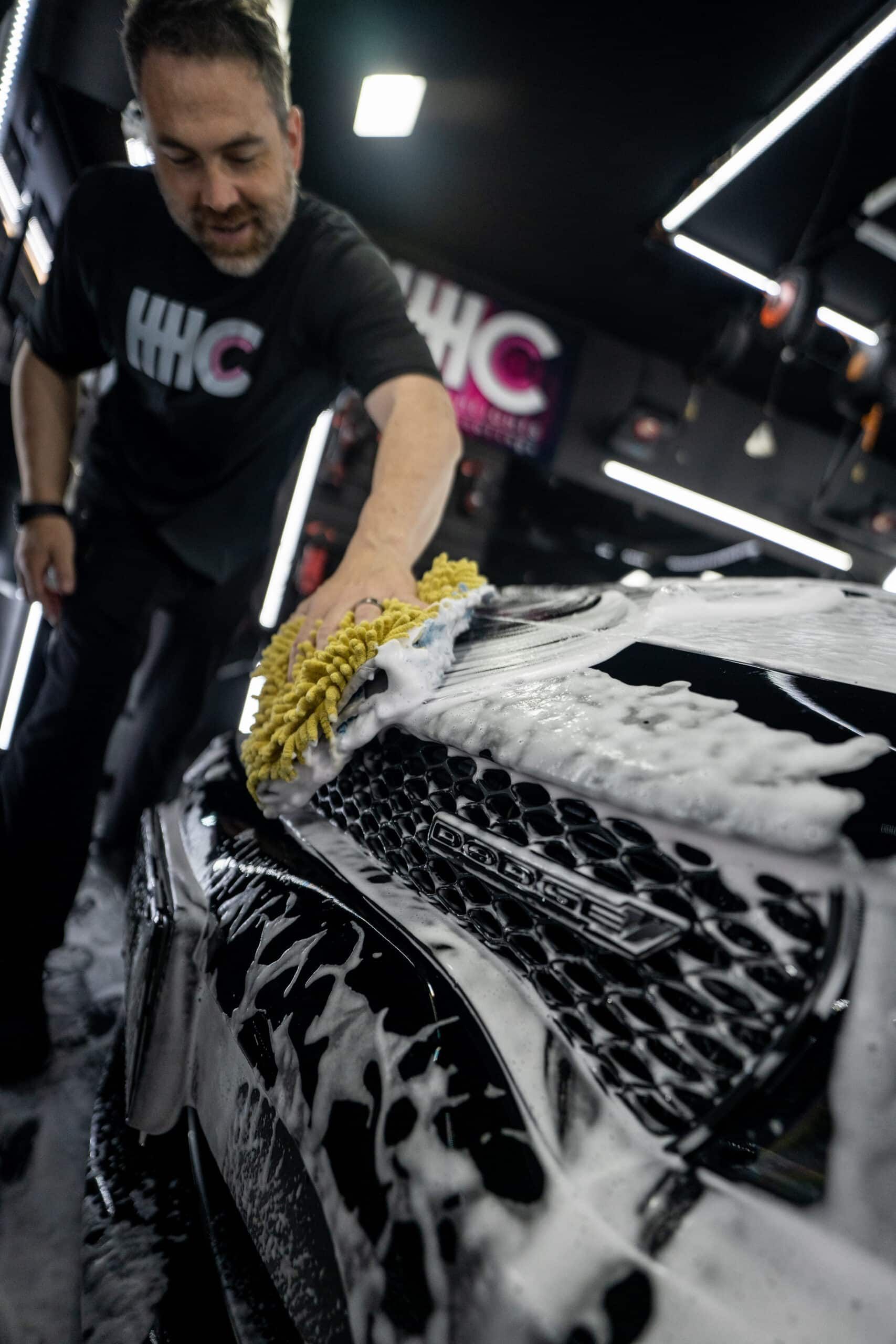 A man is washing a black and white car with a yellow sponge.