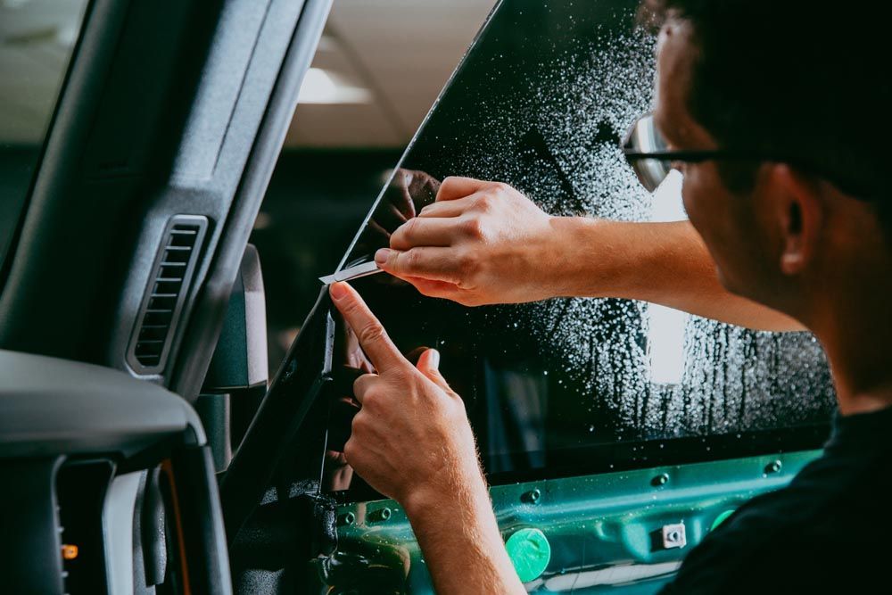 A man is cleaning the windshield of a blue car.