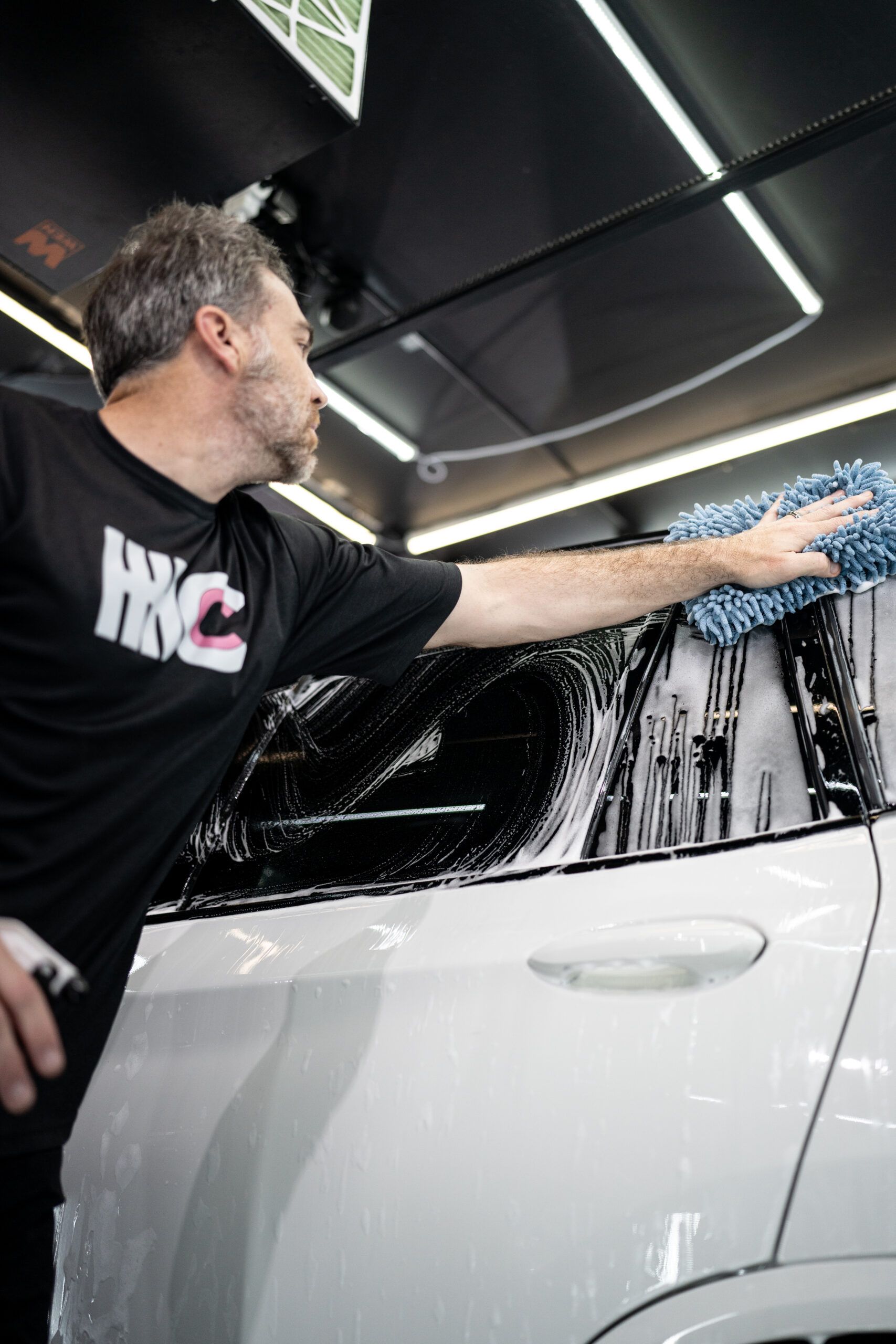 A man is washing a car with a cloth in a garage.