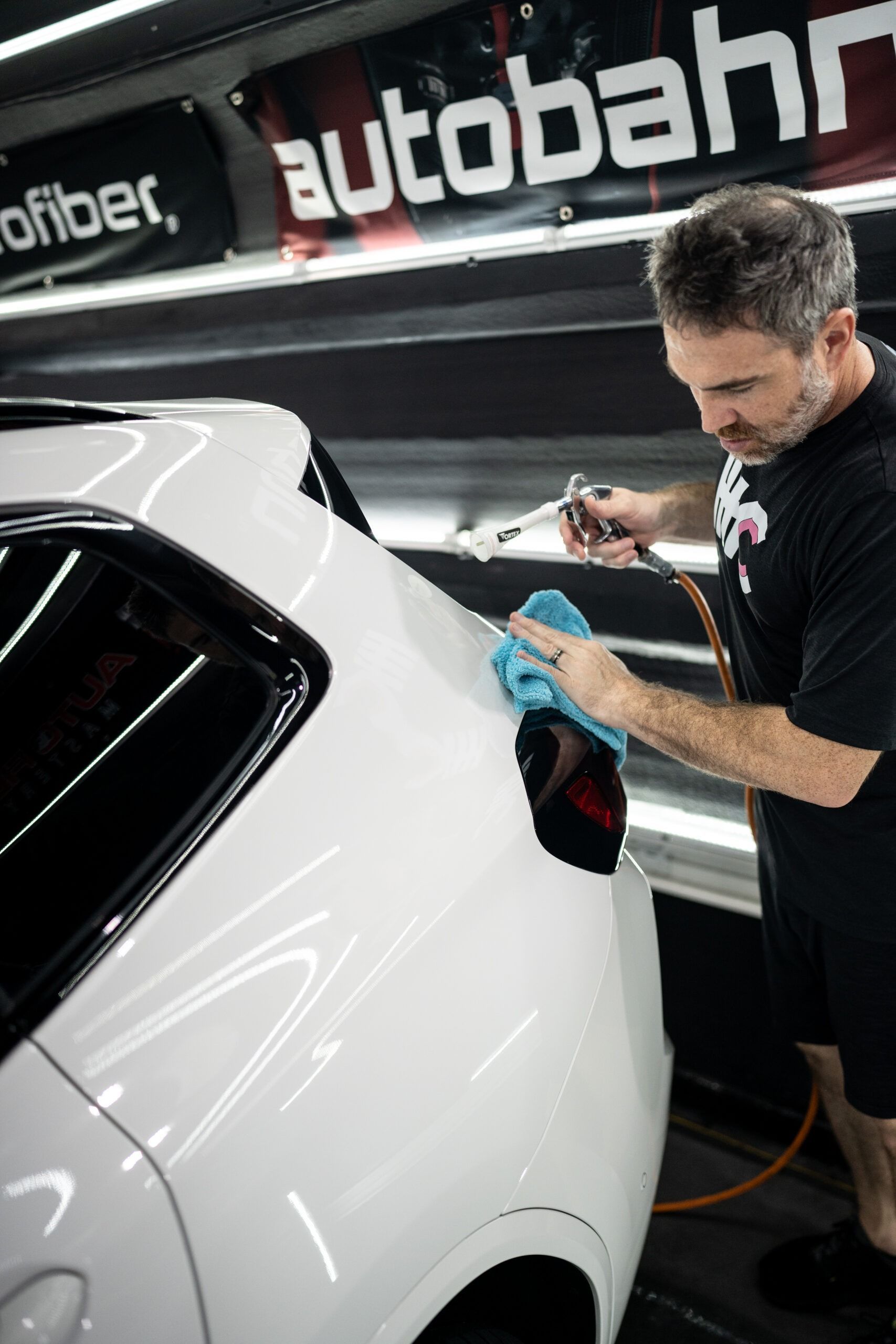 A man is cleaning a white car with a blue cloth.