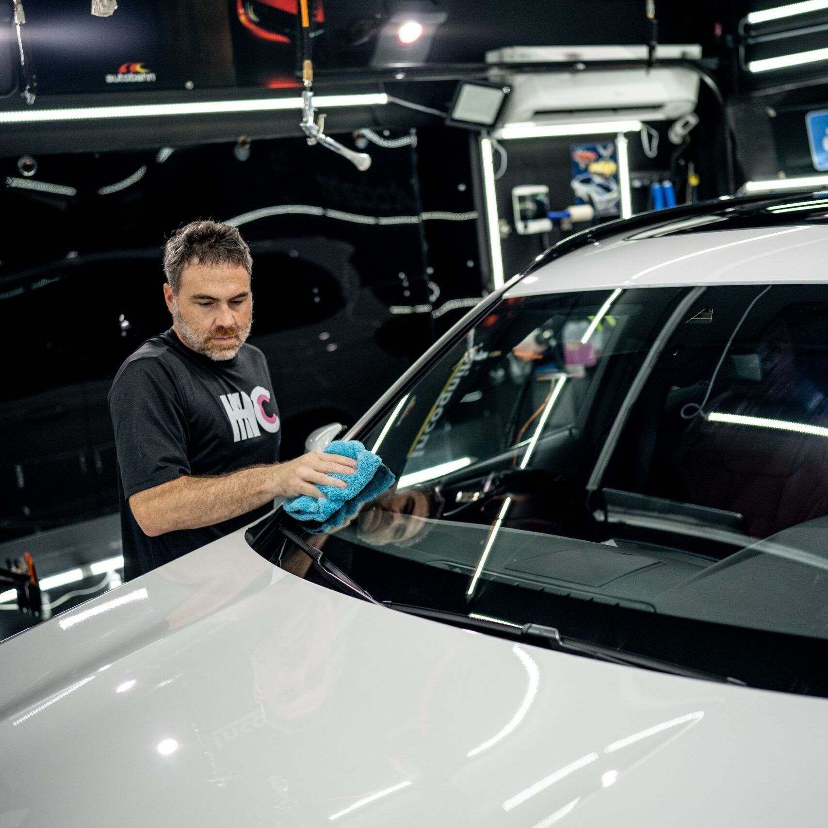 A man is cleaning the windshield of a white car in a garage.