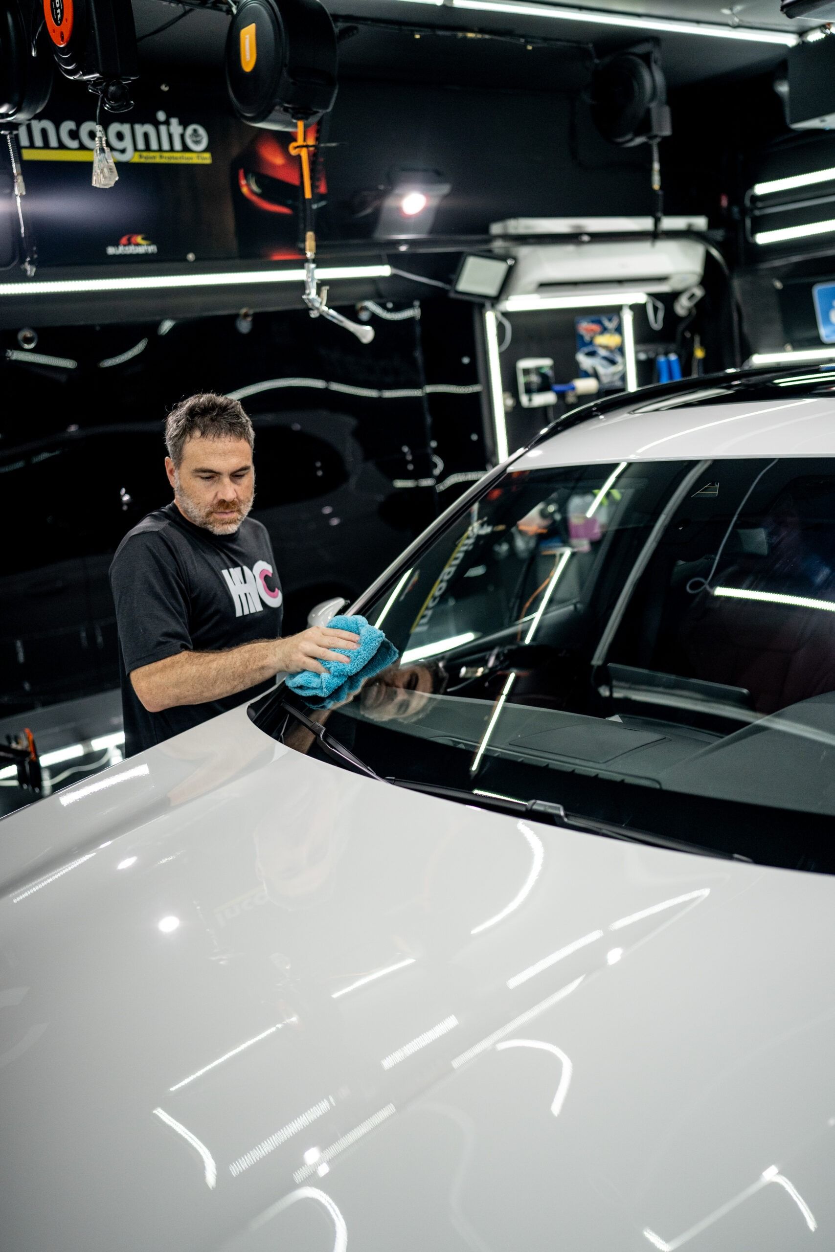 A man is cleaning the windshield of a white car in a garage.