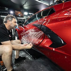 A man is wrapping a red sports car with plastic wrap.