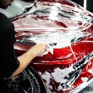 A man is washing a red car with soap and water.