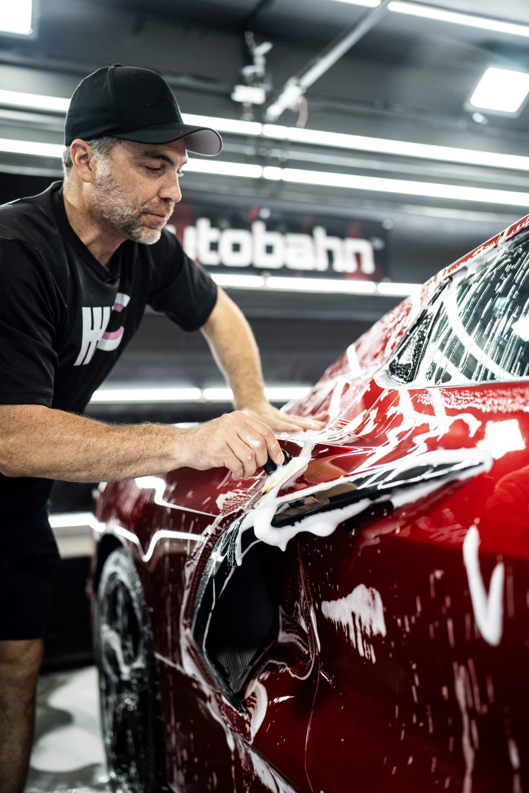 A man is washing a red car in a garage.