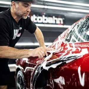 A man is washing a red car in a garage.