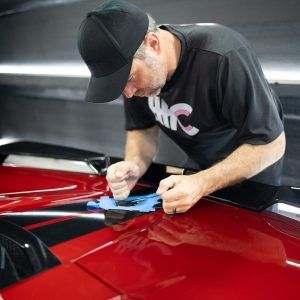 A man is working on the hood of a red car.
