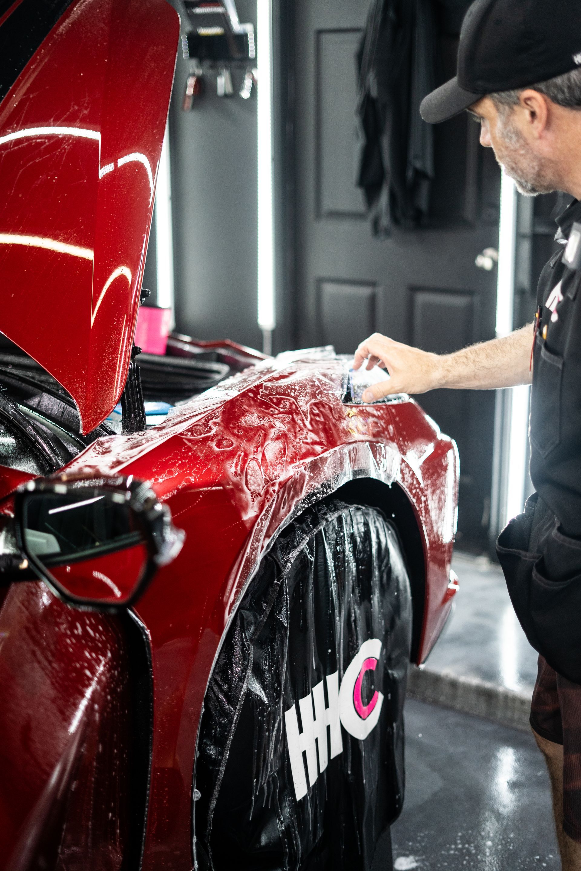 A man is cleaning the fender of a red car in a garage.