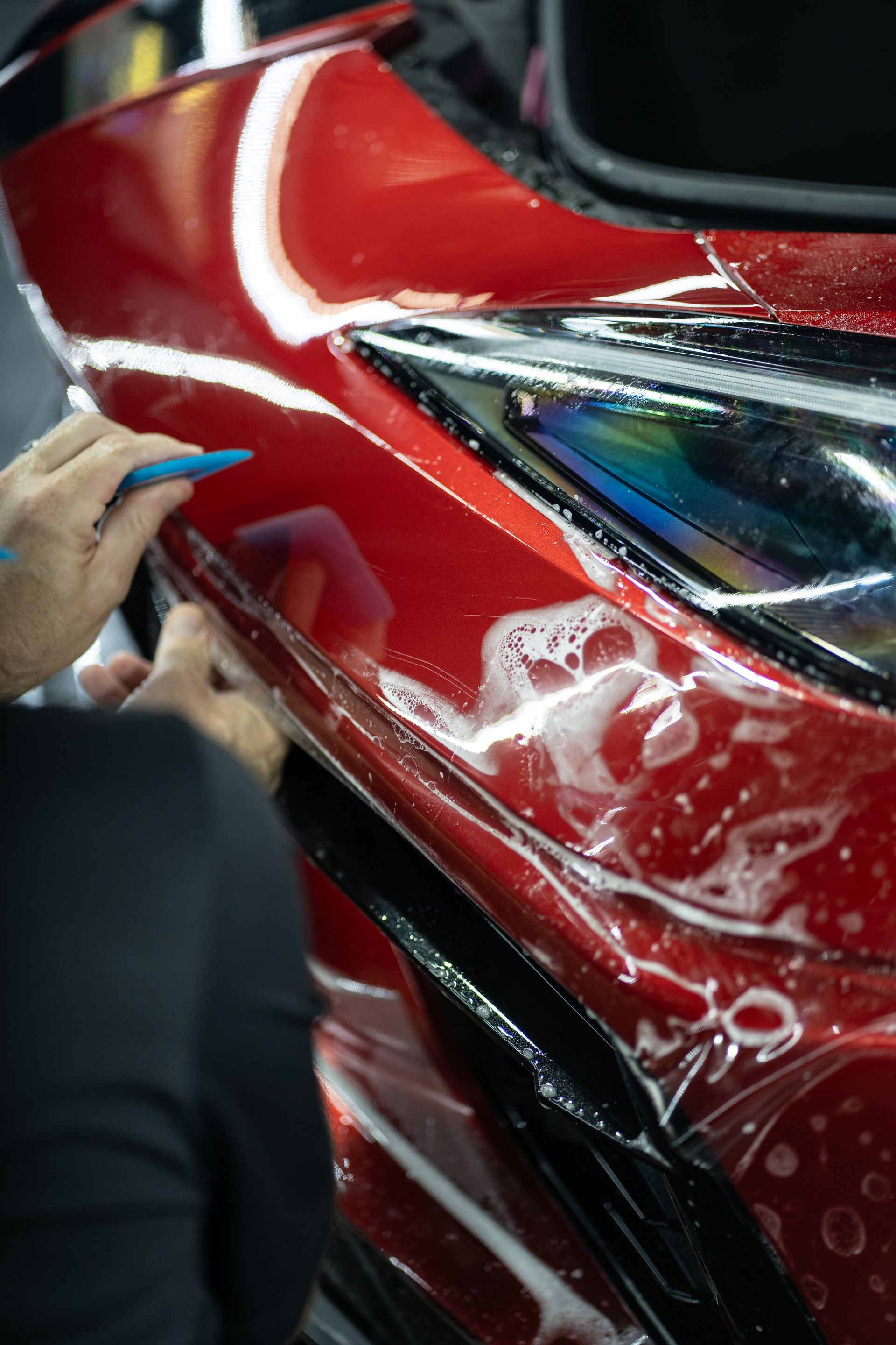 A person is applying a protective film to a red car.
