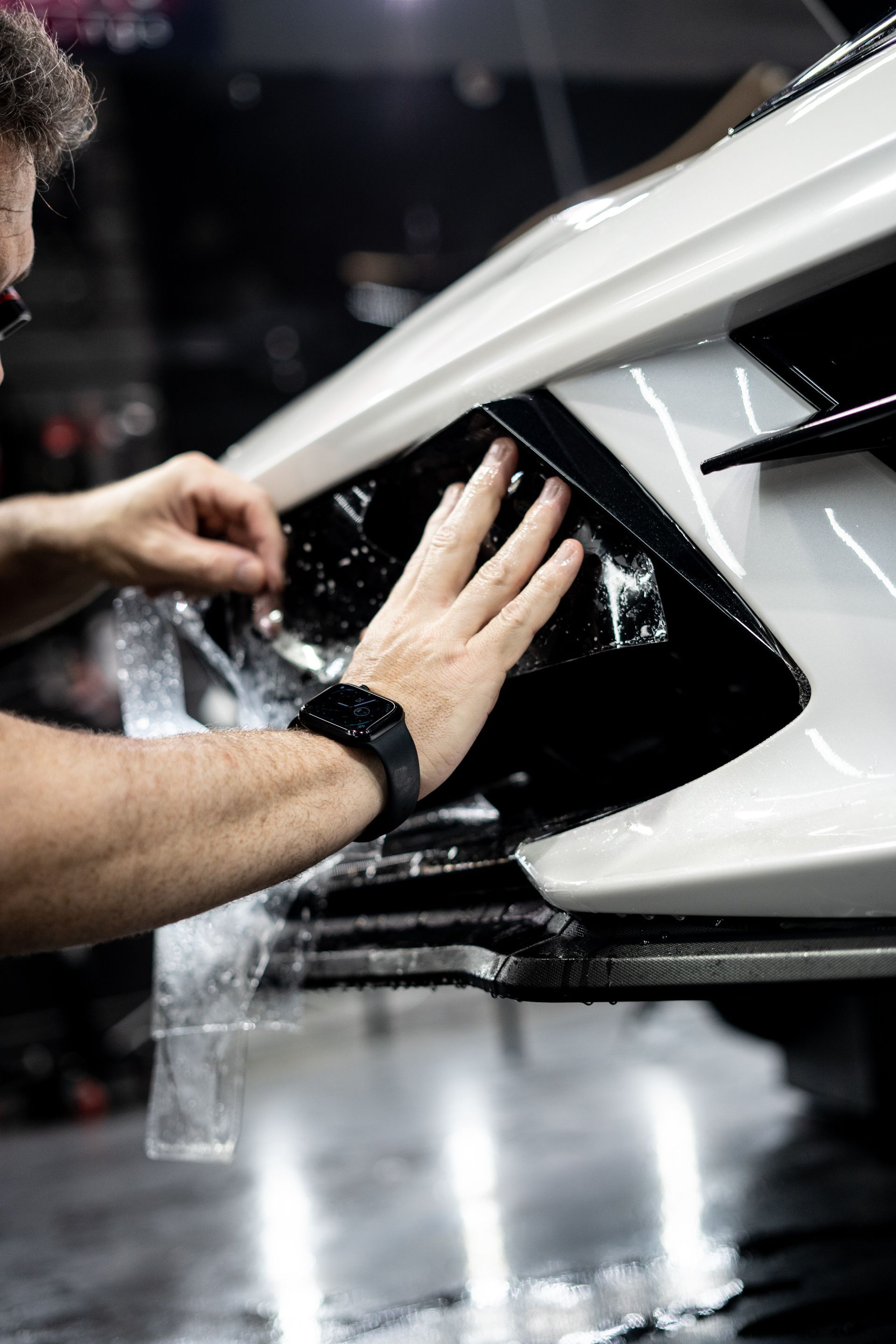 A man is applying a protective film to the front of a car.