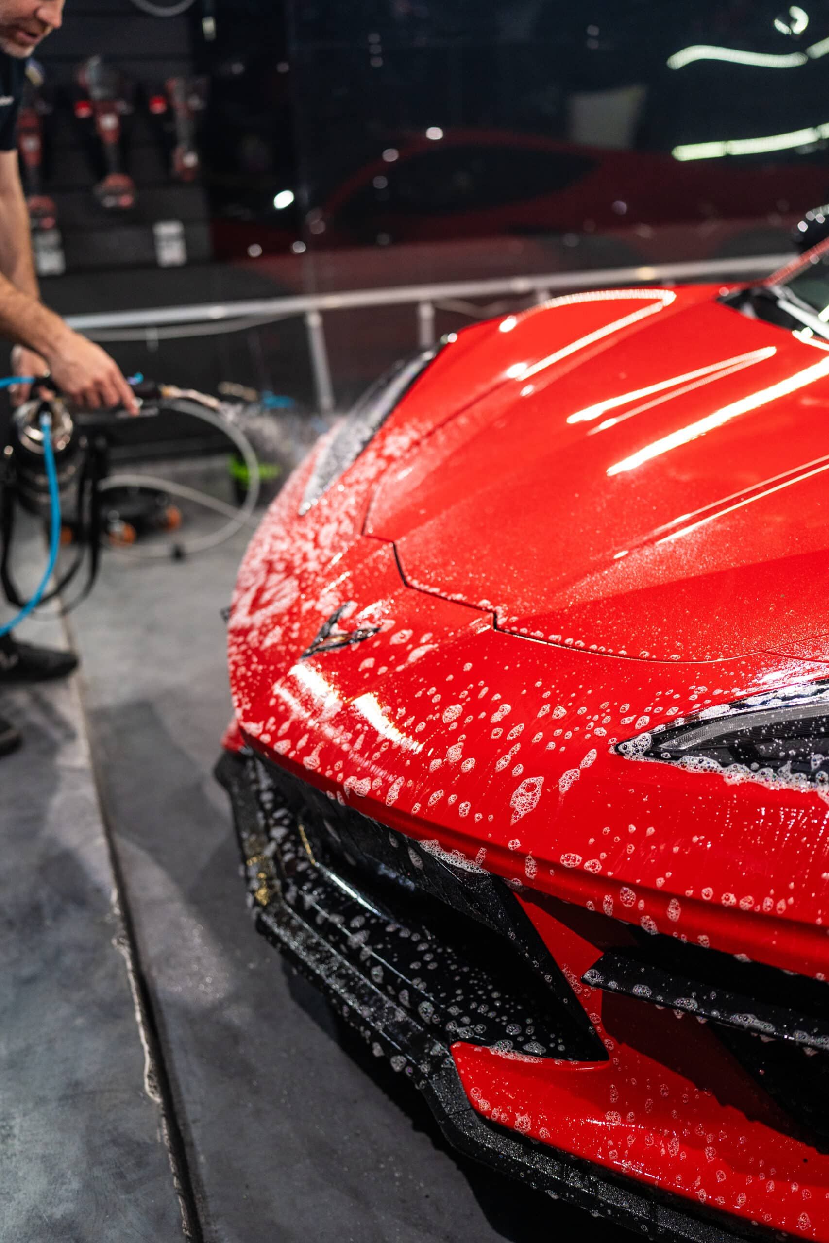 A man is washing a red sports car with a hose.