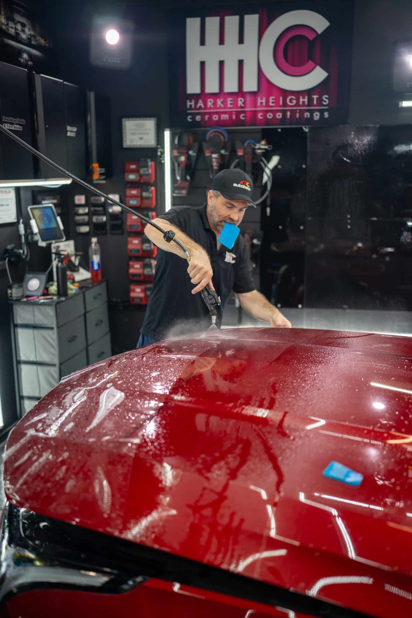 A man is polishing the hood of a red car in a garage.