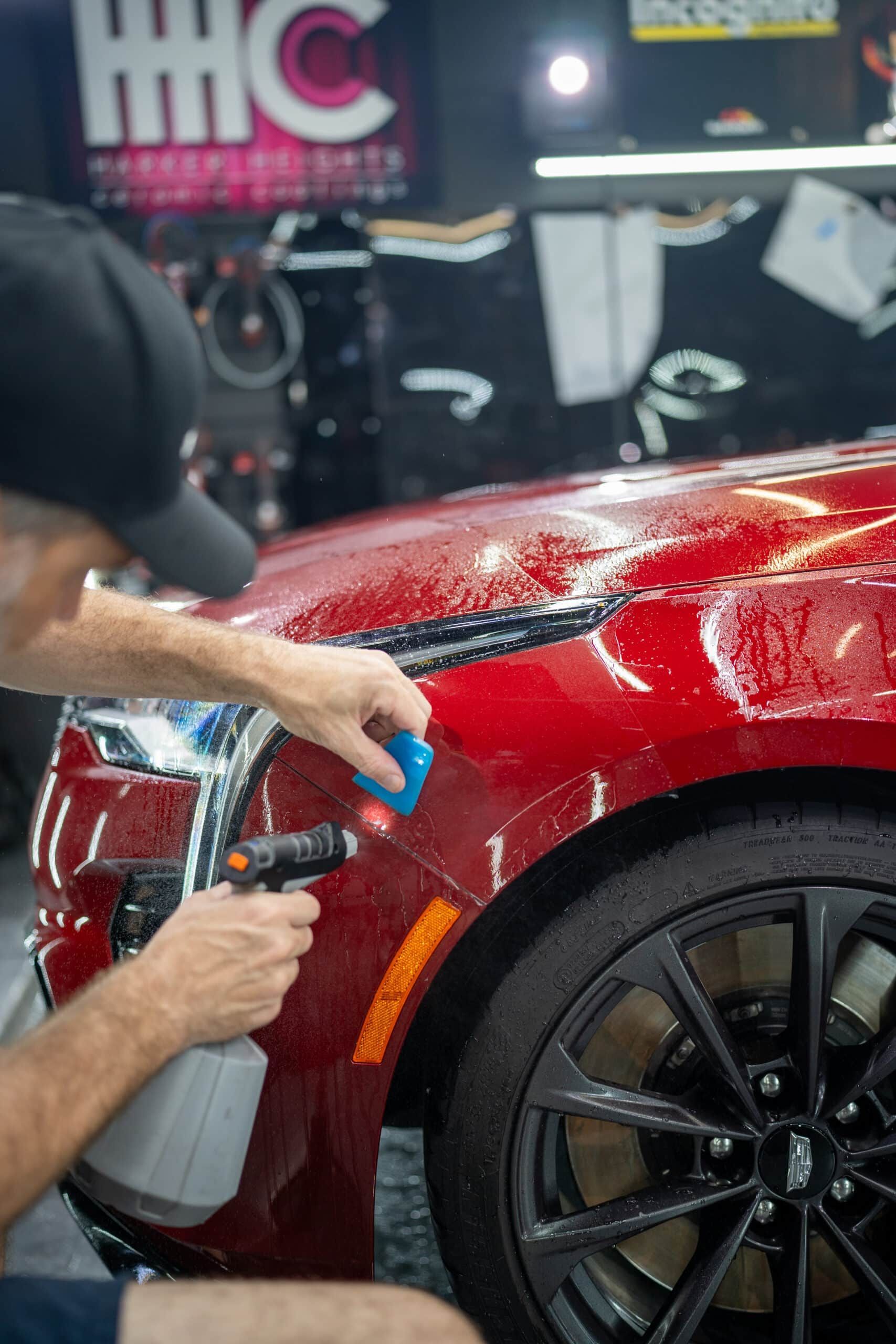 A man is polishing the fender of a red car.