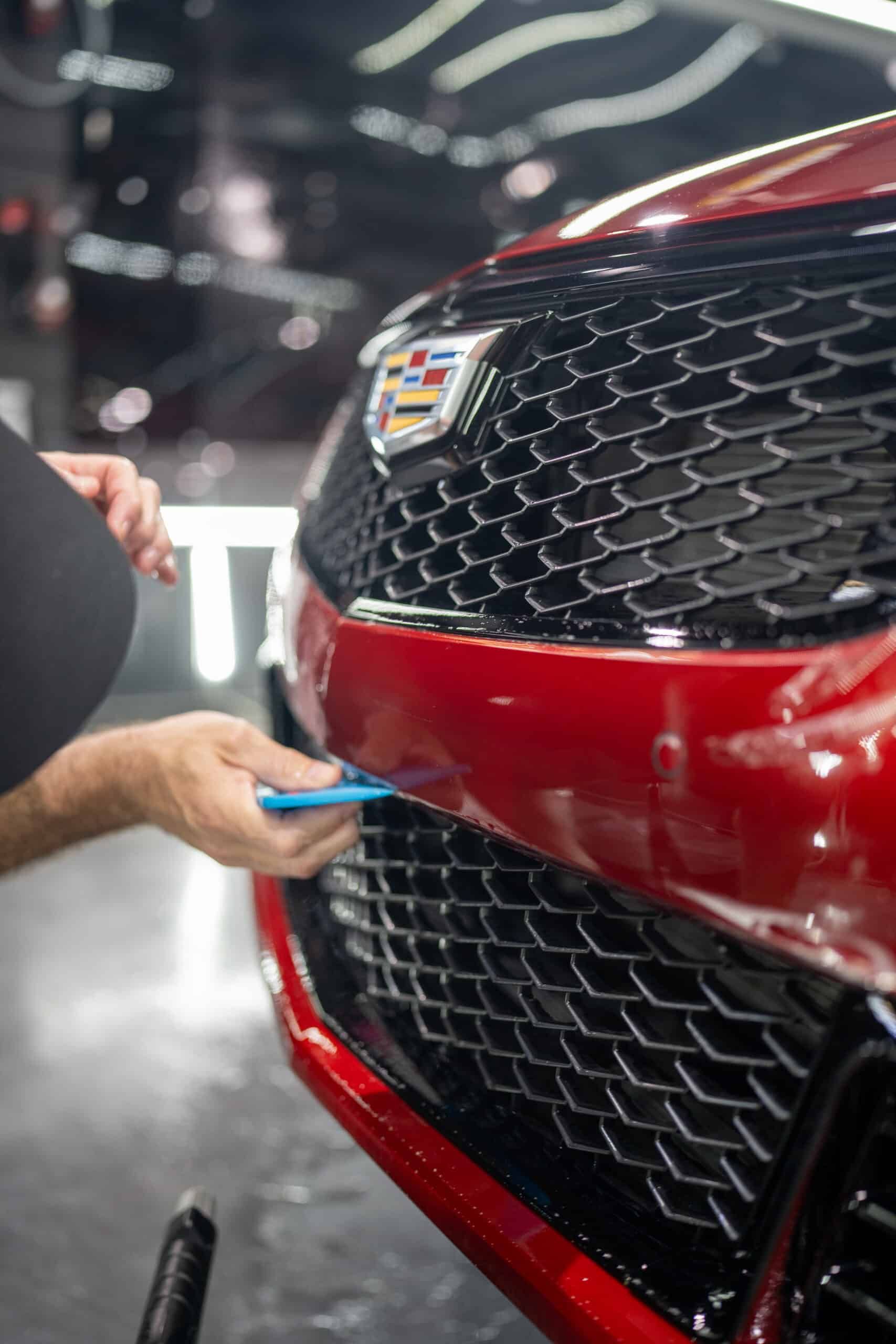 A man is applying a protective film to the front of a red cadillac.