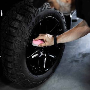 A man is cleaning a tire with a pink sponge.