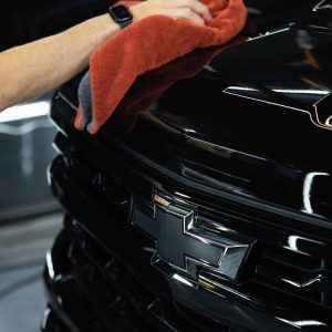 A person is cleaning a black car with a towel.