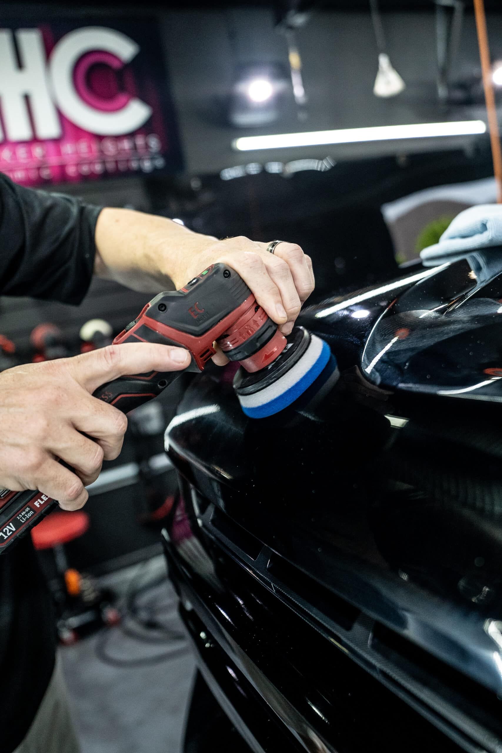 A person is polishing a black car with a machine.