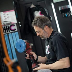 A man in a black shirt is polishing a car with a machine.