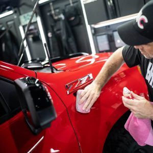A man is polishing the fender of a red truck.