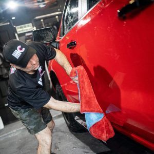A man is cleaning a red truck with a towel.