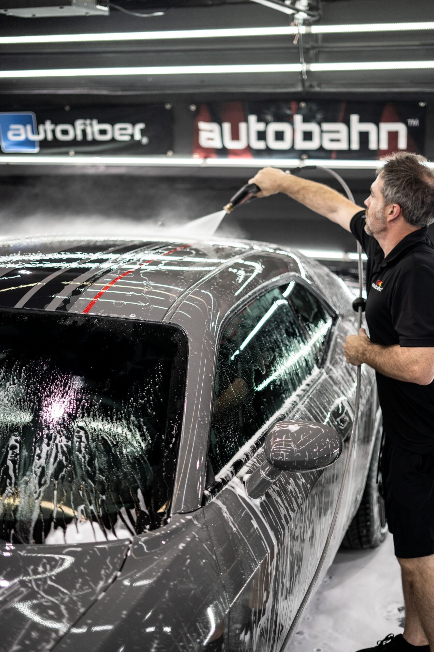 A man is washing a car with a high pressure washer.