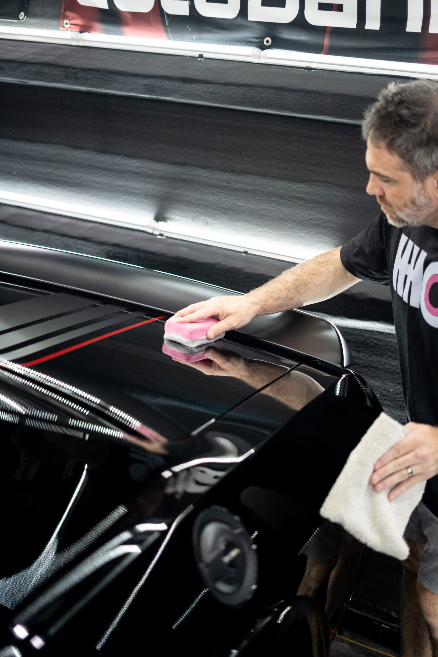A man is polishing a black car with a pink sponge.