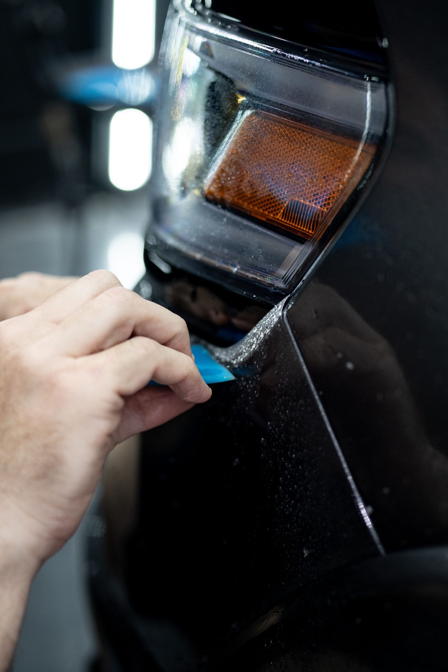 A person is applying a protective film to a car headlight.
