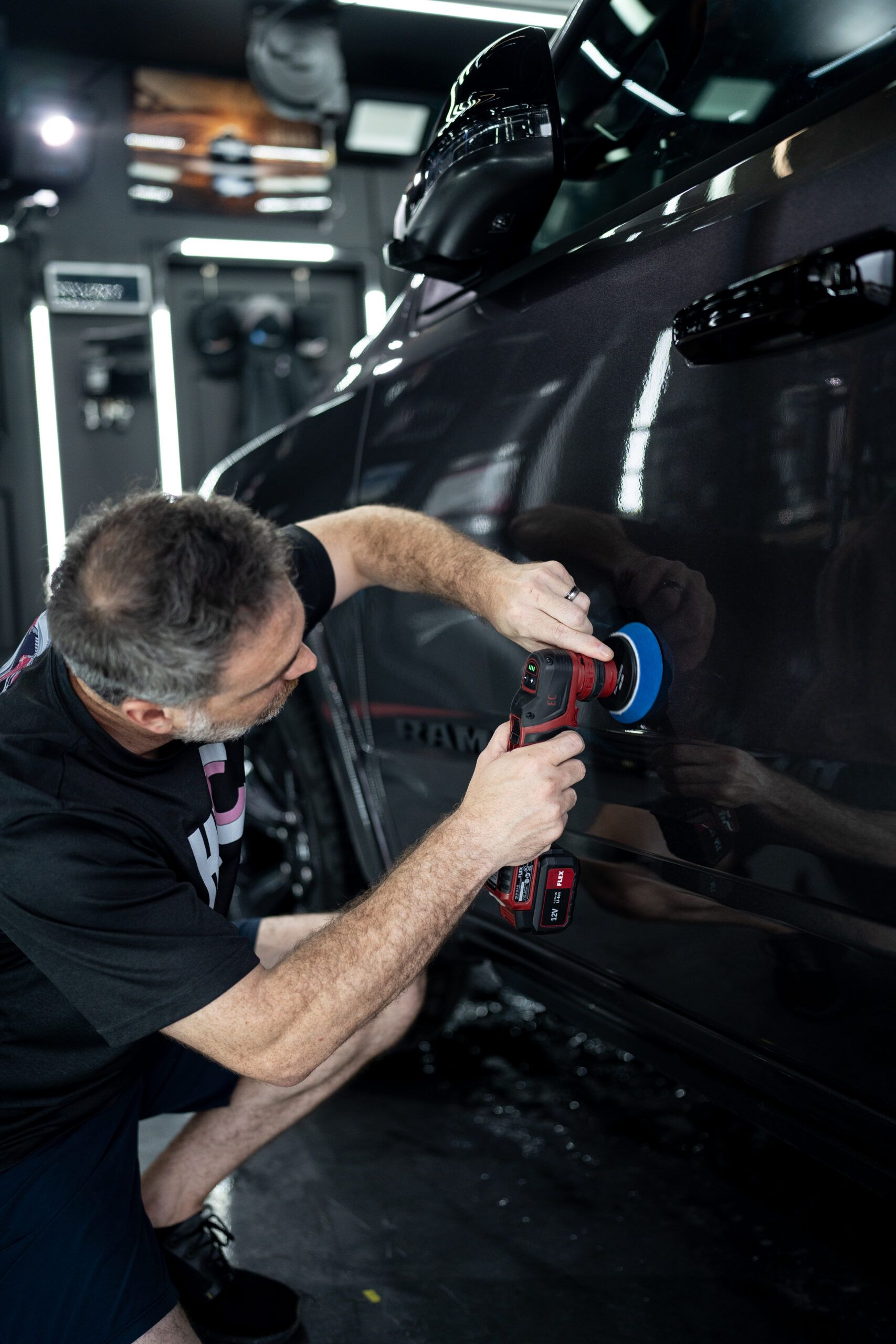 A man is polishing a car with a machine in a garage.
