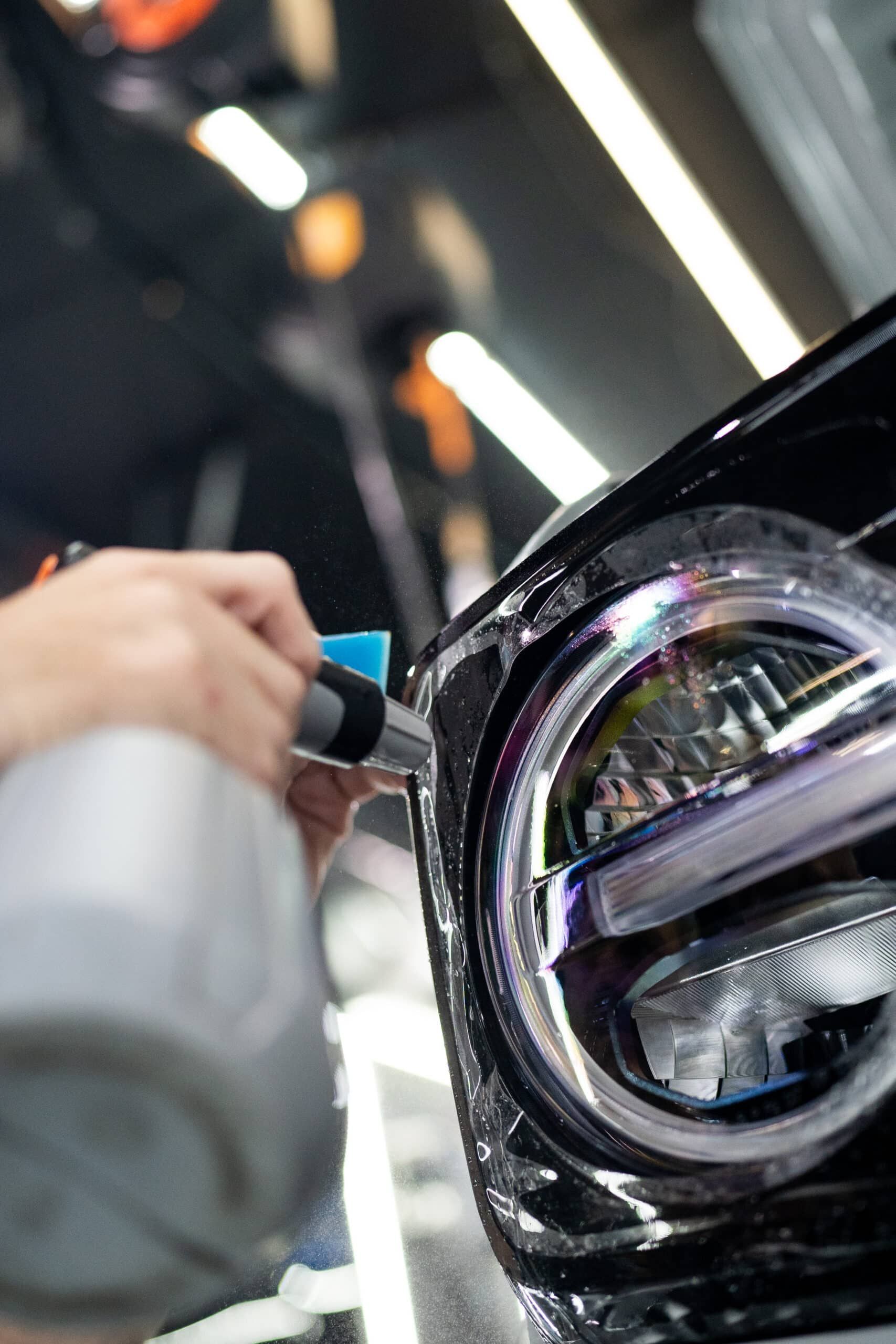 A person is applying protective film to the headlight of a car.