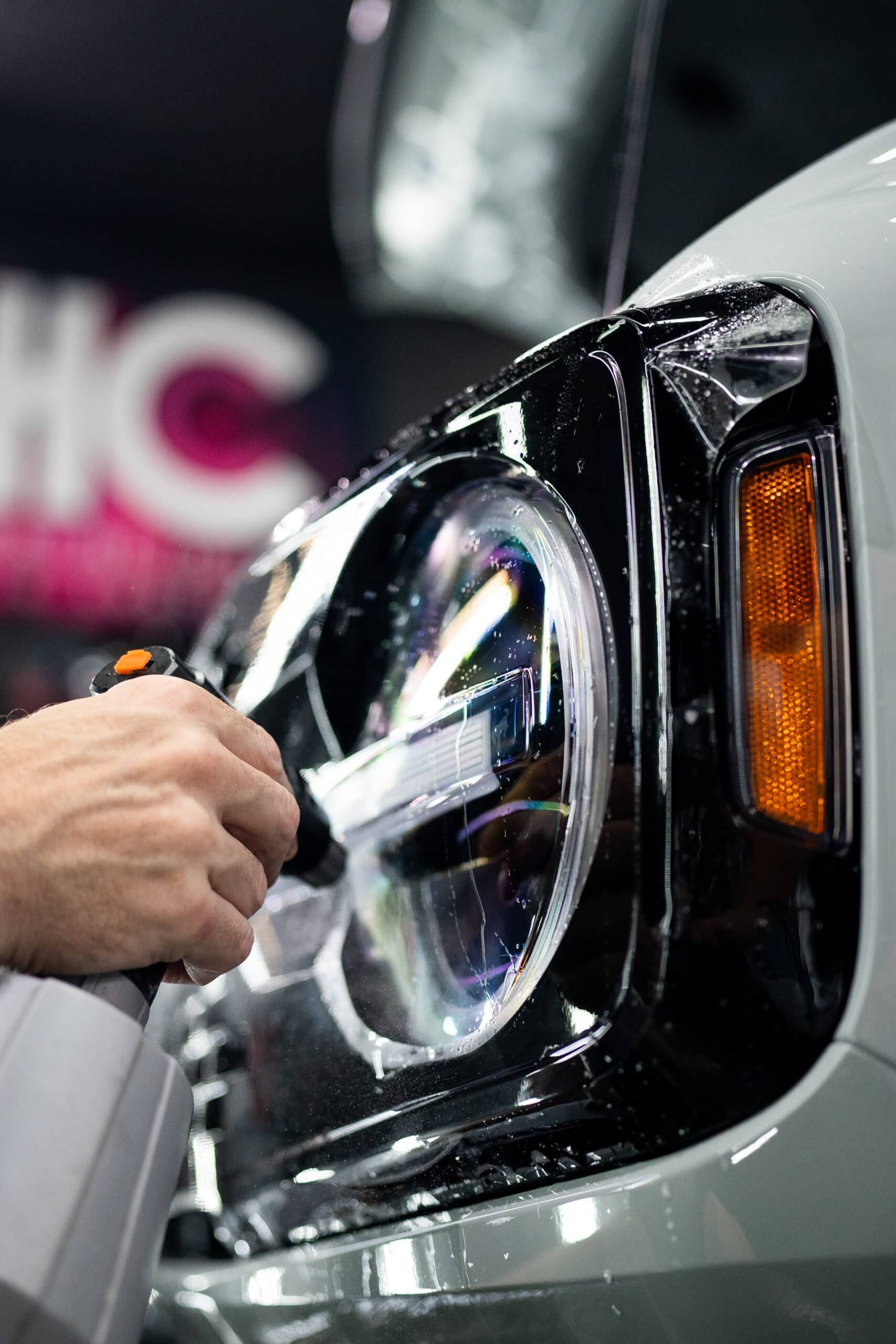 A person is applying a protective film to the headlight of a car.