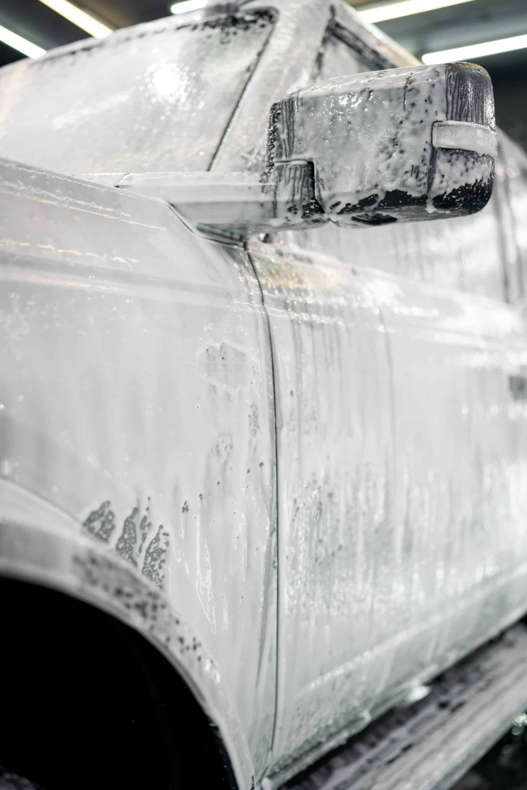 A white truck is covered in foam at a car wash.