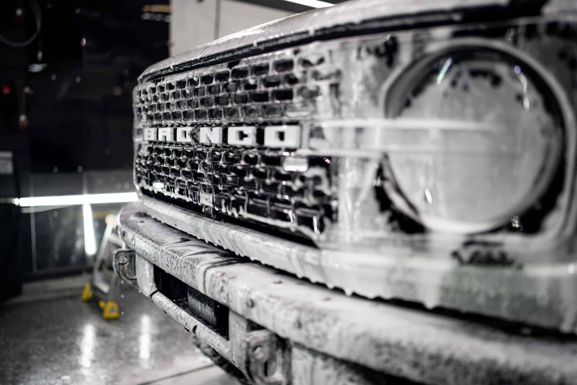 A black and white photo of a ford bronco being cleaned with foam.