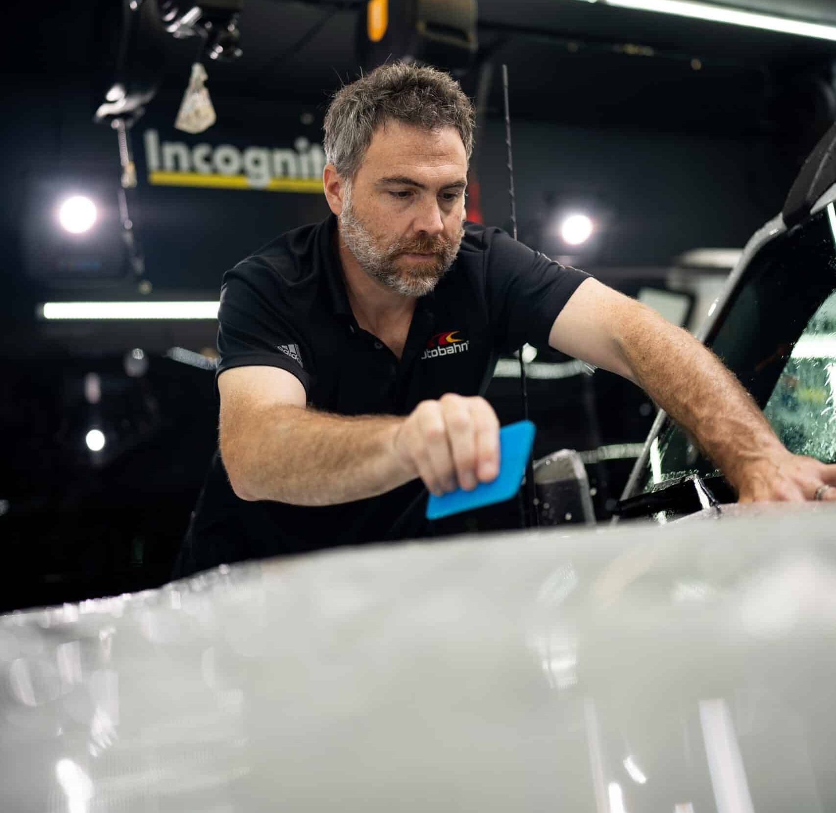 A man in a black shirt is working on a car in front of a sign that says incognito