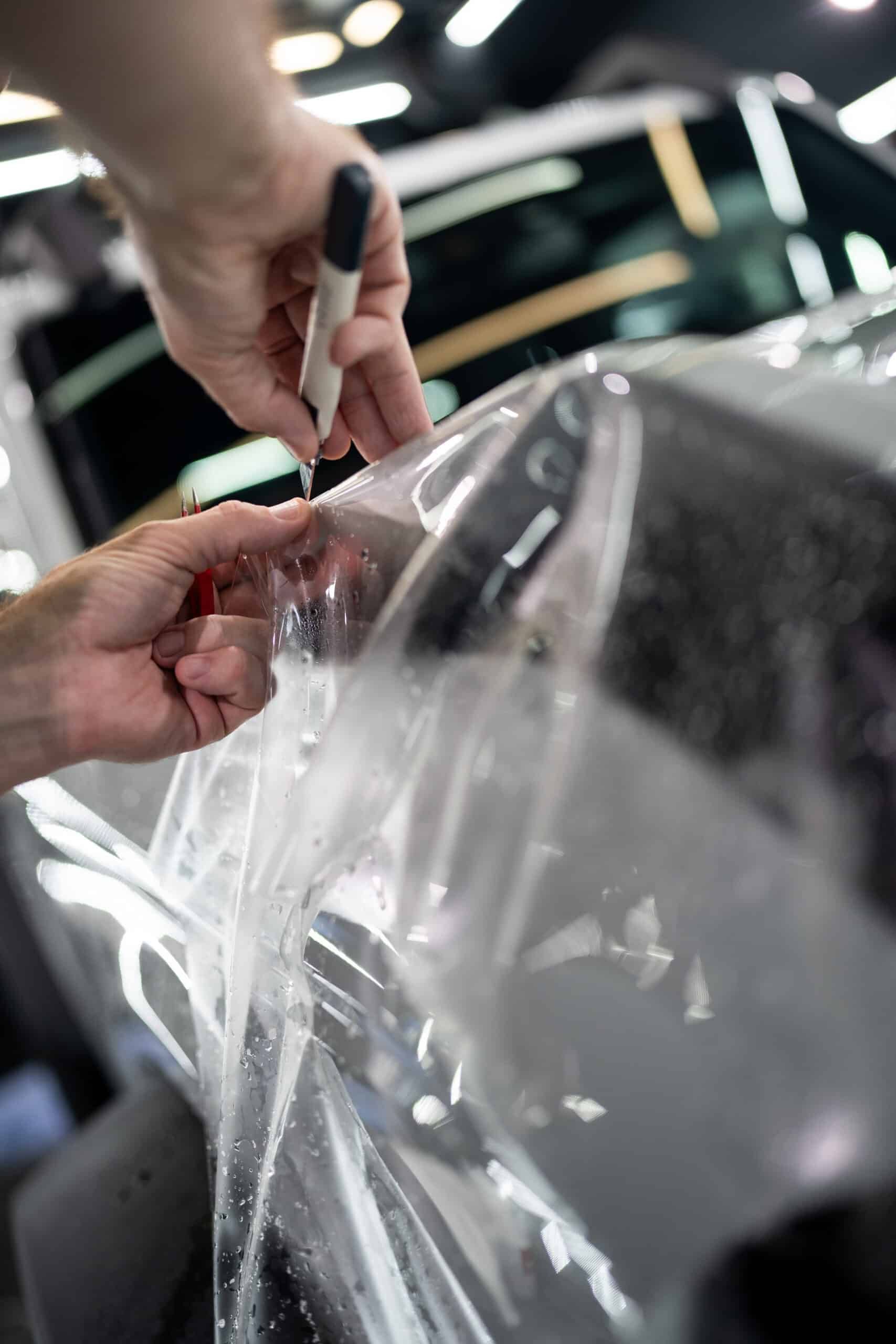 A person is applying plastic wrap to a car with a marker.