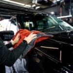 A man is cleaning a car with a towel in a garage.