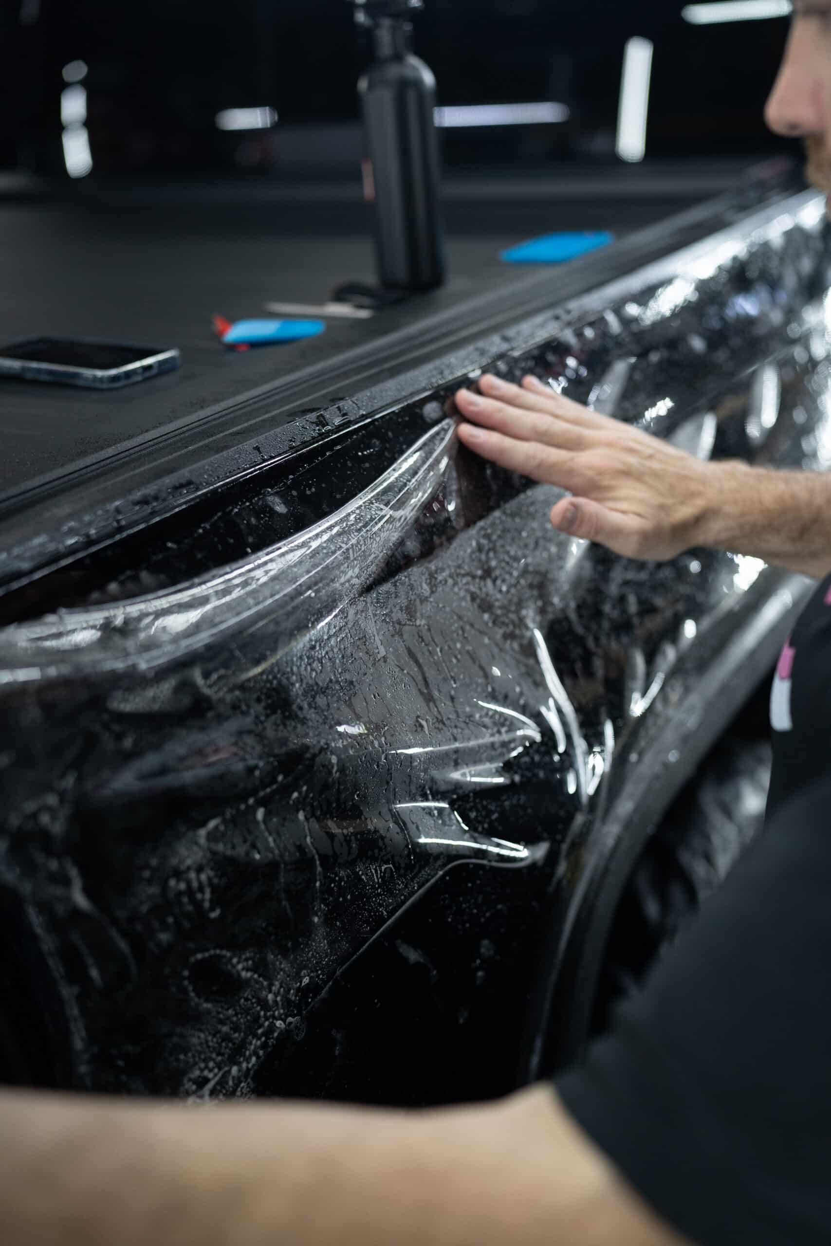 A man is wrapping a car with a clear film.