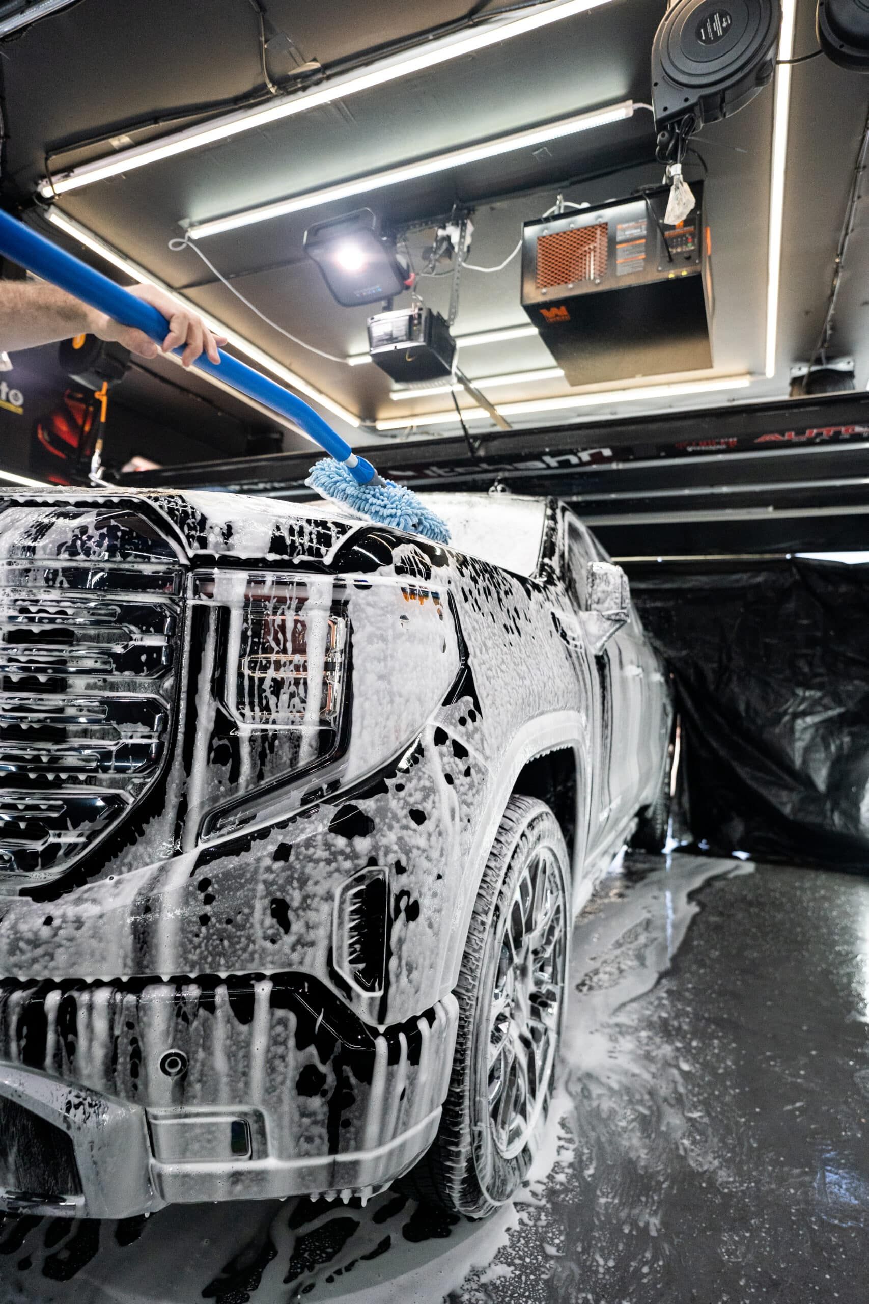 A car is covered in foam and being washed in a garage.