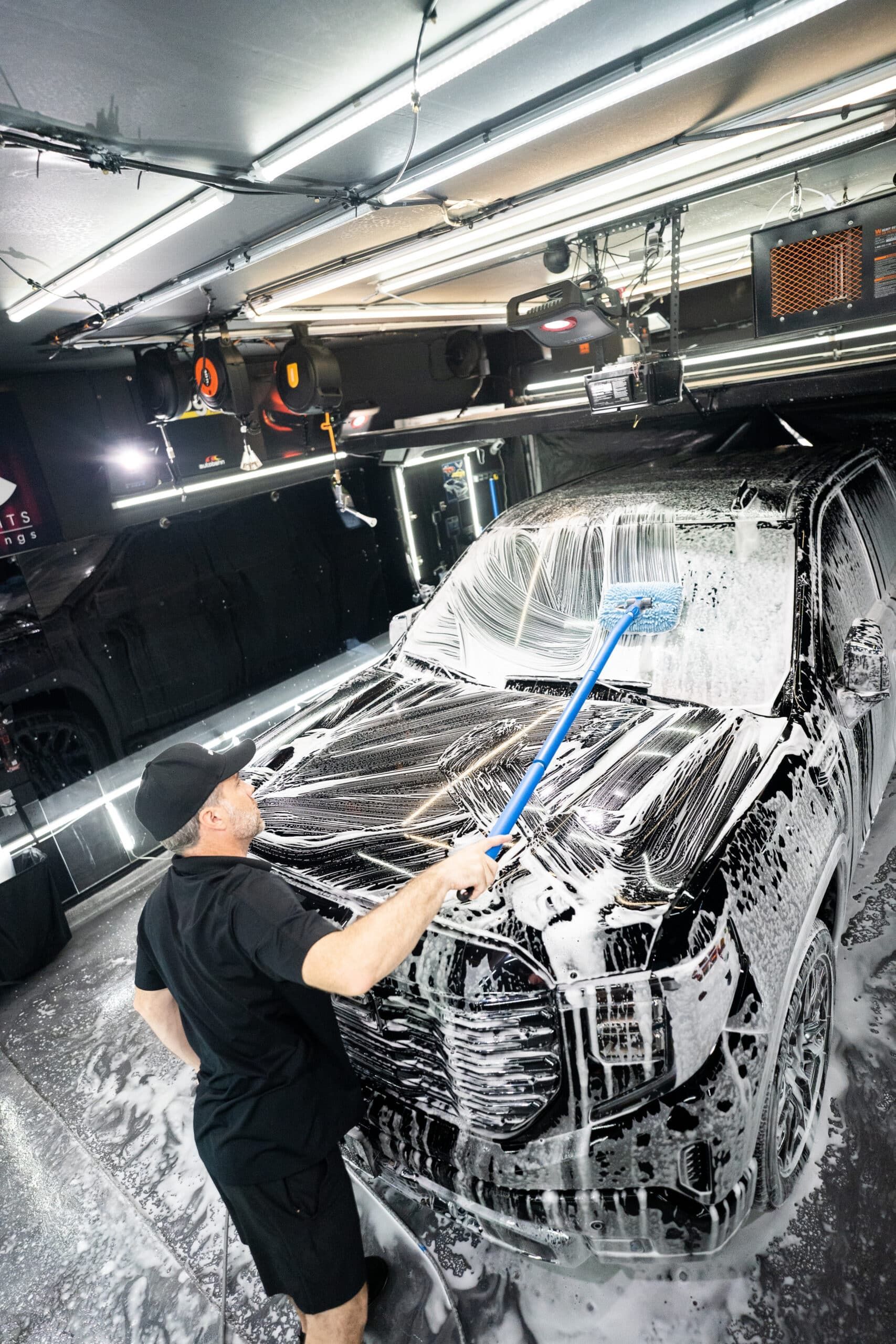 A man is washing a car with a foam brush in a garage.