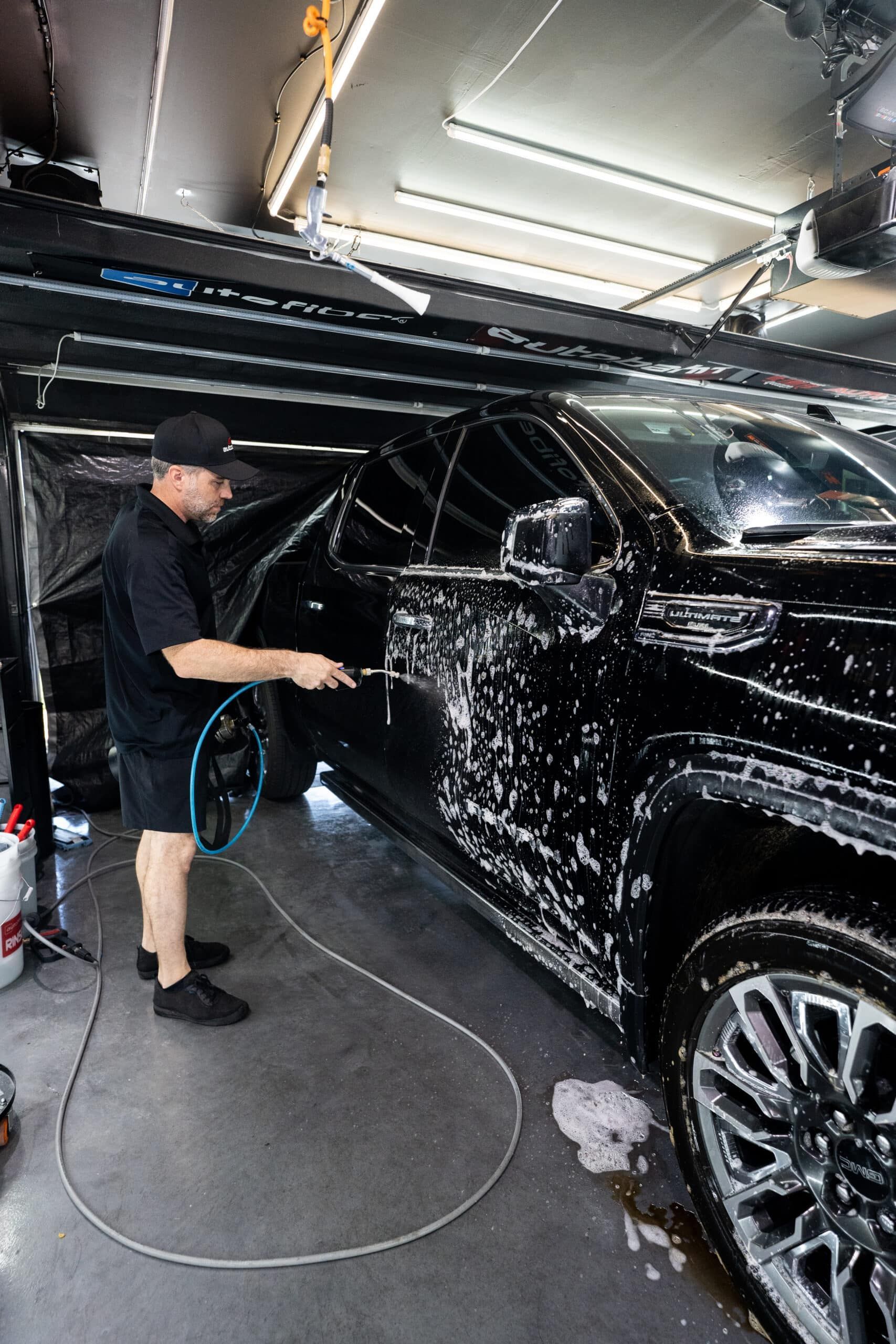 A man is washing a black car in a garage.